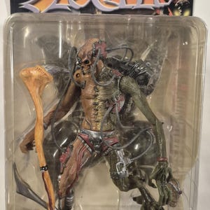 Puede incluir: Una figura de acción Todd McFarlane's Spawn en su empaque blíster original. La figura presenta un diseño esquelético y biomecánico con cables expuestos, un cuerpo texturizado en tonos bronce y verde, detalles rojos y un accesorio de bastón óseo.