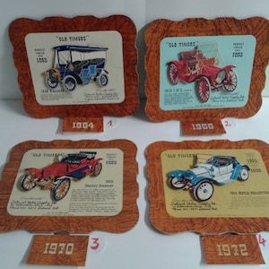 May include: Four vintage car prints, each in a wooden-look frame. The prints feature classic car illustrations with the text "OLD TIMERS" and the years 1895 and 1900. Each print has a year at the bottom: 1964, 1968, 1970, and 1972.
