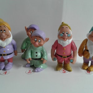 Pode incluir: Sete figuras de plástico dos sete anões do filme da Disney Branca de Neve e os Sete Anões. Os anões usam todos roupas de cores diferentes e têm expressões faciais diferentes. Os anões são numerados de 1 a 7.