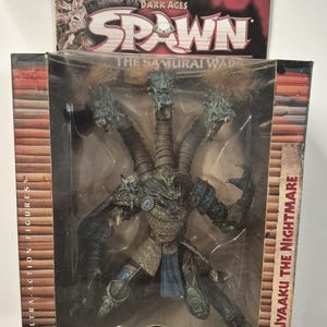 May include: McFarlane Toys Dark Ages Spawn The Samurai Wars Jyaaku the Nightmare action figure in original packaging. The figure features a multi-headed creature with textured armor, blue accents, and brown hair elements inside a display box.