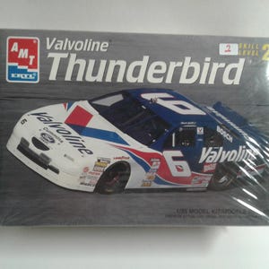 Pu&ograve; includere: Un kit di modelli in scatola di un'auto da corsa Valvoline Thunderbird. L'auto &egrave; bianca, blu e rossa con il numero 6 sul lato. La scatola presenta il logo AMT ERTL e le parole "Valvoline Thunderbird". Il kit &egrave; di livello 2.