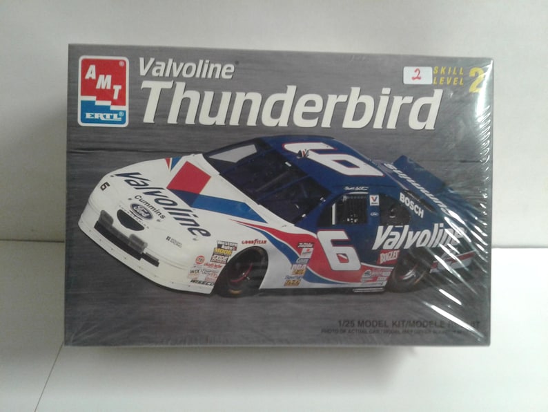 Pu&ograve; includere: Un kit di modelli in scatola di un'auto da corsa Valvoline Thunderbird. L'auto &egrave; bianca, blu e rossa con il numero 6 sul lato. La scatola presenta il logo AMT ERTL e le parole "Valvoline Thunderbird". Il kit &egrave; di livello 2.