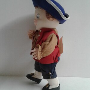 Pu&ograve; includere: Bambola vintage vestita con un abito in stile coloniale. La bambola indossa un cappello blu con finiture bianche, un gilet rosso e pantaloni blu scuro. Le scarpe della bambola sono nere con dettagli dorati. Il viso della bambola &egrave; dipinto.