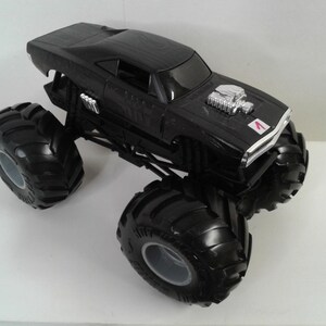 May include: Black monster truck toy with large tyres and a detailed engine. The toy car features a black body with silver engine detailing and a small red and white emblem on the front.