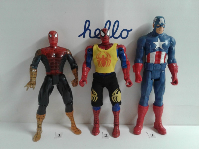 May include: Three action figures, two Spider-Man figures and one Captain America figure. The Spider-Man figures are wearing red and blue suits with a spider logo. The Captain America figure is wearing a blue and red suit with a white star on the chest. The figures are standing on a white surface.