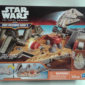 May include: A Star Wars Micro Machines Millennium Falcon playset box. The box features a brown and gray playset with a red and gray tower. A white Millennium Falcon spaceship is flying over the playset. The box also features a smaller image of the Millennium Falcon spaceship on the side. The box is labeled "Star Wars The Force Awakens Micro Machines Millennium Falcon Playset."