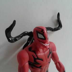 Pode incluir: Figura de a&ccedil;&atilde;o vermelha e preta de um super-her&oacute;i com um grande sorriso de dentes. A figura tem um ap&ecirc;ndice preto em forma de tent&aacute;culo na cabe&ccedil;a.