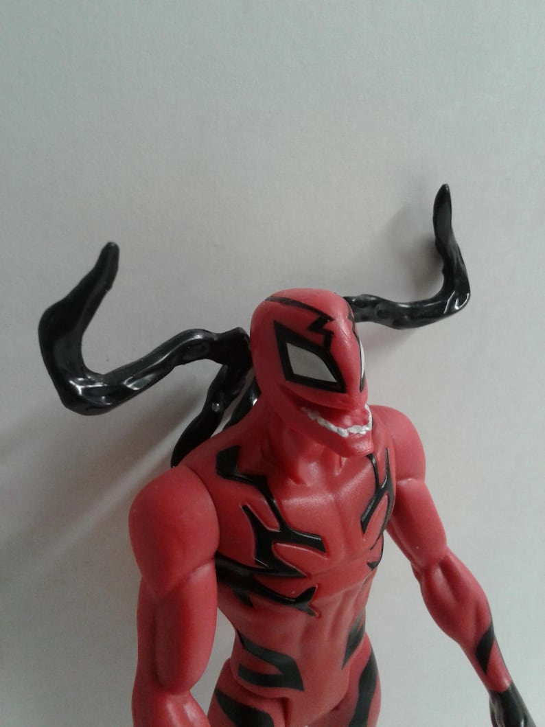Pode incluir: Figura de a&ccedil;&atilde;o vermelha e preta de um super-her&oacute;i com um grande sorriso de dentes. A figura tem um ap&ecirc;ndice preto em forma de tent&aacute;culo na cabe&ccedil;a.