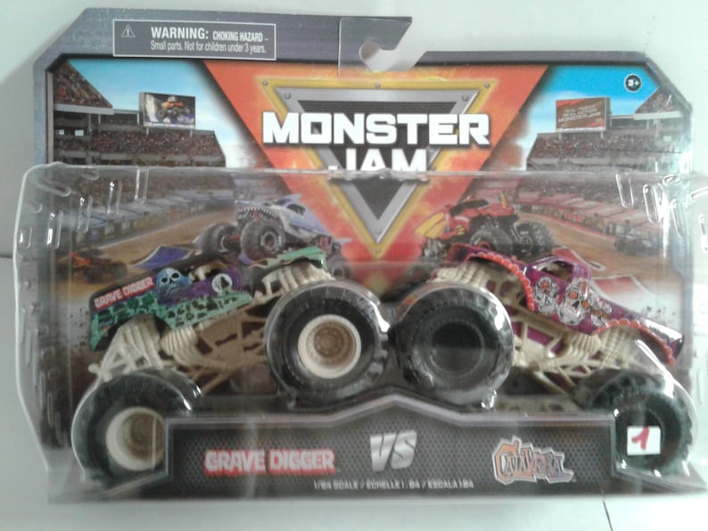 May include: A packaged Monster Jam toy set featuring two monster trucks: Grave Digger and El Toro Loco. The Grave Digger truck is green and black with a skull design, while El Toro Loco is red and purple. The package includes the text "Grave Digger VS El Toro Loco".