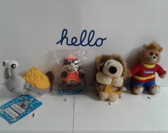 May include: Four plush toys, numbered 1 through 4.  Toy 1 is a gray snail with a yellow shell. Toy 2 is a brown and orange squirrel holding a can of orange soda. Toy 3 is a brown hedgehog holding a yellow letter L. Toy 4 is a brown bear wearing a red and yellow shirt with the word "Extrême" on it.