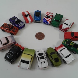 Puede incluir: Una colección de coches de juguete coloridos dispuestos en círculo alrededor de una moneda. Los coches son de varios colores, incluyendo rojo, verde, azul y blanco, con algunos diseños únicos. Un tema divertido y lúdico.