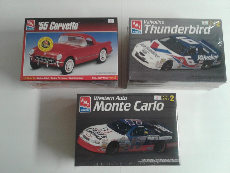 Pu&ograve; includere: Sono esposti tre kit di modellini di auto. La scatola in alto a sinistra presenta una '55 Corvette rossa. La scatola in alto a destra mostra un'auto da corsa Valvoline Thunderbird. La scatola in basso mostra un'auto da corsa Western Auto Monte Carlo.