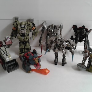 以下が含まれることがあります： 緑と黒のロボット、銀色のロボット、黒と銀のロボット、茶色と銀のロボット、赤と黒のロボット、黒と銀のロボット、赤と黒のロボットなど、7体のトランスフォーマーアクションフィギュアのコレクションです。