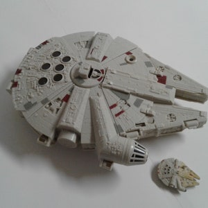 Könnte beinhalten: Ein weißes und graues Plastikmodell des Raumschiffs Millennium Falcon aus Star Wars. Das Modell hat rote Akzente und ein separates, kleineres Modell der Fluchtkapsel des Millennium Falcon.