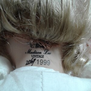 May include: Vintage Madison Lee doll with blonde hair and a white dress. The doll has a label on the back of its neck that reads "Madison Lee Vintage 2067.1999".