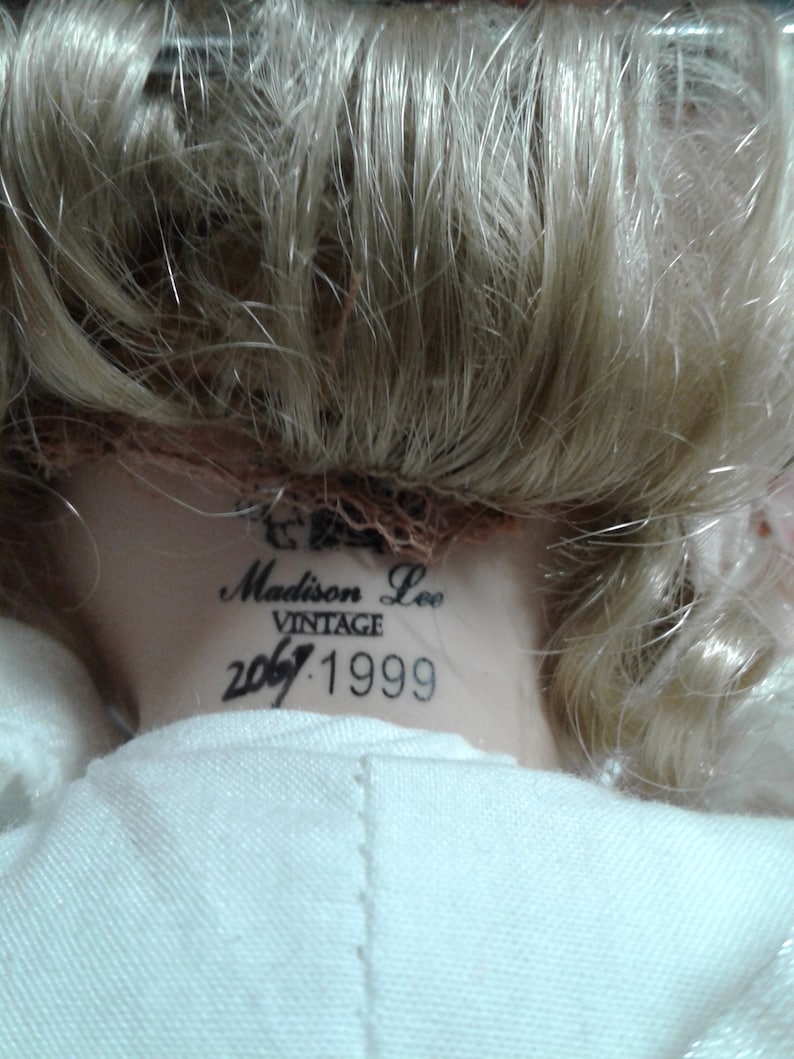May include: Vintage Madison Lee doll with blonde hair and a white dress. The doll has a label on the back of its neck that reads "Madison Lee Vintage 2067.1999".