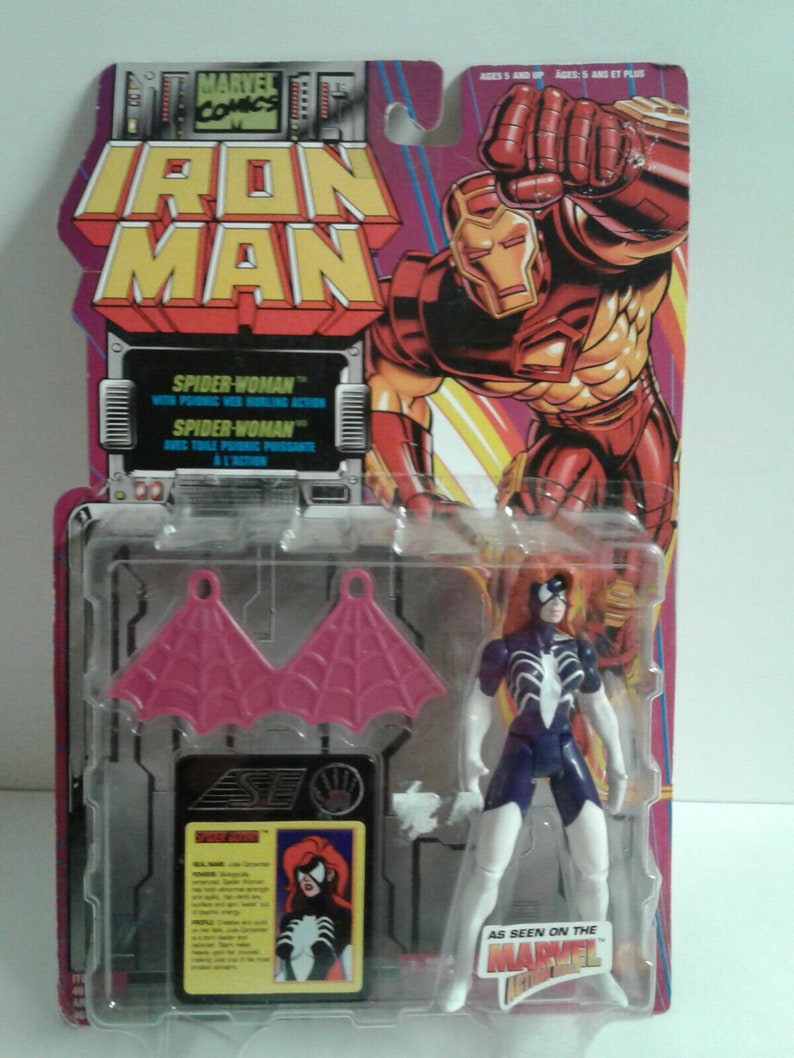May include: A Spider-Woman action figure with red hair, a blue and white suit, and pink wings. The figure is packaged in a plastic blister pack with a cardboard backing featuring Iron Man and the text "Marvel Comics Iron Man".