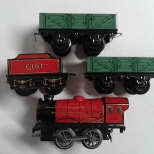 May include: A collection of vintage toy train cars and a locomotive. The train cars are green and red with black wheels. The locomotive is red with black accents. The number 6161 is visible on one of the cars.