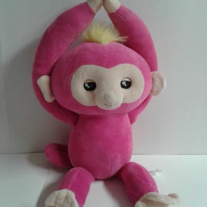 May include: Pink plush monkey toy with yellow hair sitting with its arms raised above its head.