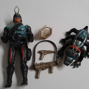 May include: A blue and black action figure with a silver helmet and a red and black belt. The figure is holding a silver gun. There is a silver and black bug-like creature with red accents, a silver shield, and two silver guns.