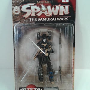 Puede incluir: Figura de acción de McFarlane Toys de la serie Dark Ages Spawn: The Samurai Wars. La figura es de una guerrera samurái femenina con armadura negra, sosteniendo una espada y una lanza. El embalaje incluye el logotipo de Spawn y el texto "Spawn.com".