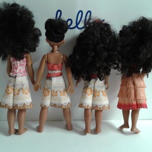 May include: Four dolls with long, curly black hair, wearing different outfits. The dolls are all wearing skirts and tops. The dolls are standing in a row, facing away from the camera.