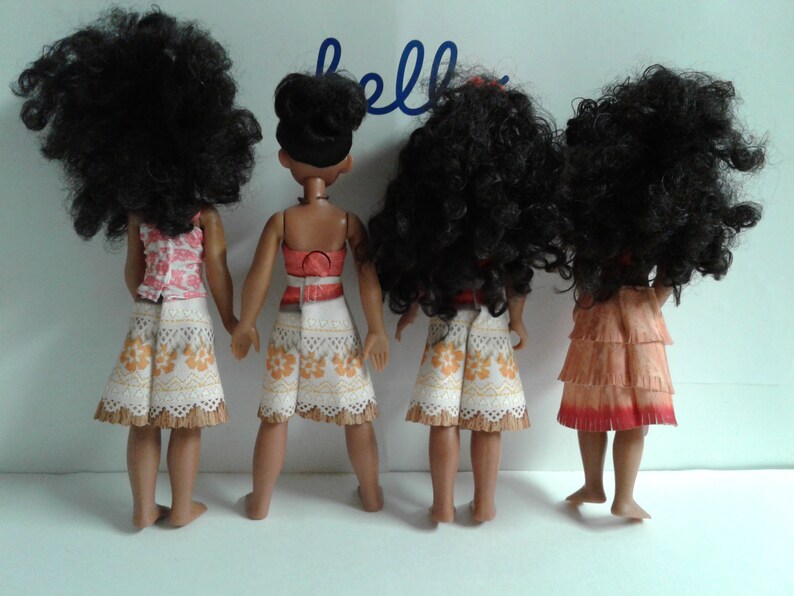 May include: Four dolls with long, curly black hair, wearing different outfits. The dolls are all wearing skirts and tops. The dolls are standing in a row, facing away from the camera.