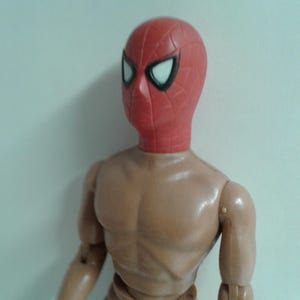 Op de afbeelding: Een rood en zwart plastic actifiguur hoofd met een wit spinnenweb ontwerp. Het hoofd is bevestigd aan een bruin plastic lichaam.