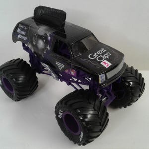 May include: Black and purple toy monster truck with large tyres. The truck features the text "Great Clips" and "Mohawk Warrior". The tyres have the text "BKT". The truck has a black mohawk on top.