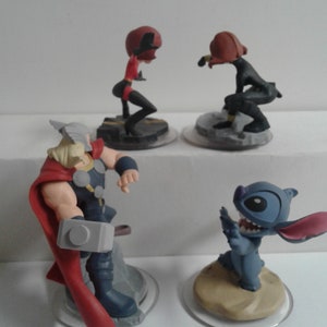 May include: Four Disney Infinity figures: a red and black superhero, a black superhero, a blue and white Stitch character, and a Thor character with a red cape and a silver hammer.