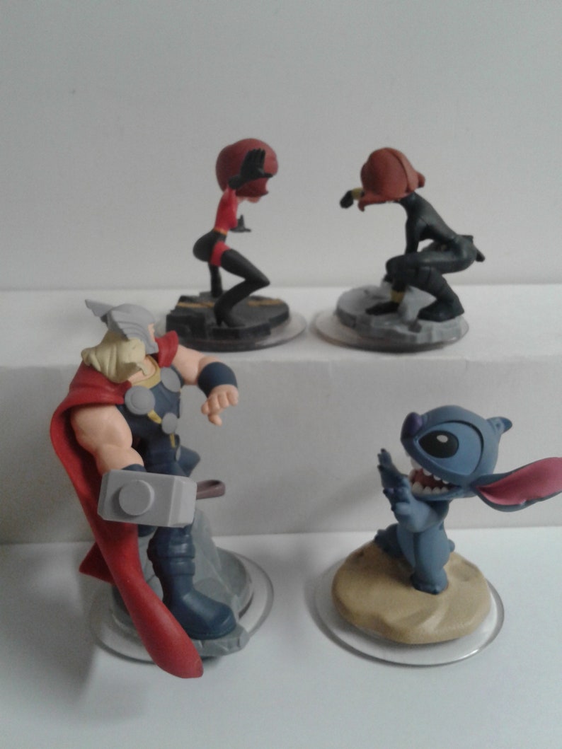 May include: Four Disney Infinity figures: a red and black superhero, a black superhero, a blue and white Stitch character, and a Thor character with a red cape and a silver hammer.