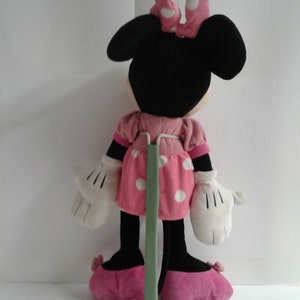 May include: A pink and white polka dot dress with a black bow on top of the head. The plush toy is standing on a green stand.