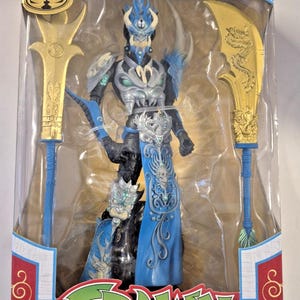 Puede incluir: Una figura de acción de Mandarin Spawn de la colección McFarlane Gold Label, dentro de una caja con ventana. La figura presenta una armadura azul y negra, una falda azul decorada con una calavera y dos grandes armas doradas con motivos de dragón.