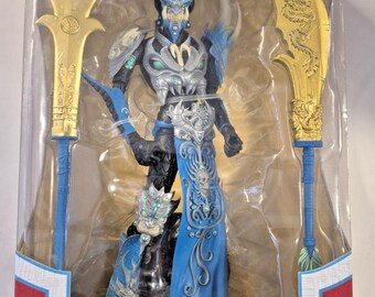 May include: A Mandarin Spawn action figure from the McFarlane Gold Label Collection, encased in a window box. The figure features blue and black armor, a skull-adorned blue skirt, and two large gold-colored polearm weapons with dragon motifs.