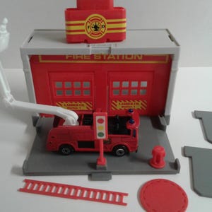 May include: A red fire station playset with a white fire truck, a ladder, and a red fire hydrant. The fire station has a sign that says "Fire Station" and a ladder company sign that says "Ladder Co. Station 1".
