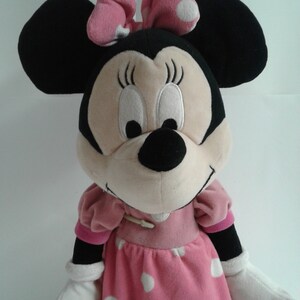May include: A plush toy of Minnie Mouse wearing a pink dress with white polka dots and a pink bow with white polka dots.