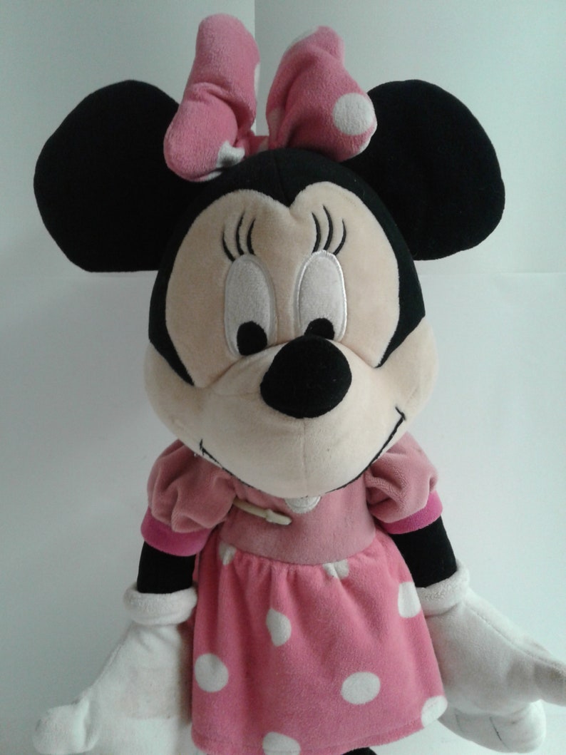May include: A plush toy of Minnie Mouse wearing a pink dress with white polka dots and a pink bow with white polka dots.