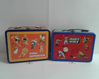 Puede incluir: Dos fiambreras vintage de metal con imágenes de atletas jugando diferentes deportes. La fiambrera azul y roja tiene el texto "Sports Afield". La otra fiambrera es roja y azul y tiene el texto "Pro Sports".