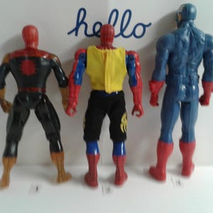 May include: Three action figures, two Spider-Man figures and one Captain America figure, standing back to back. The Spider-Man figures are wearing red and blue suits with black accents. The Captain America figure is wearing a blue and red suit with a white star on the chest.