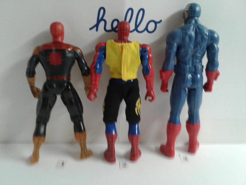 May include: Three action figures, two Spider-Man figures and one Captain America figure, standing back to back. The Spider-Man figures are wearing red and blue suits with black accents. The Captain America figure is wearing a blue and red suit with a white star on the chest.