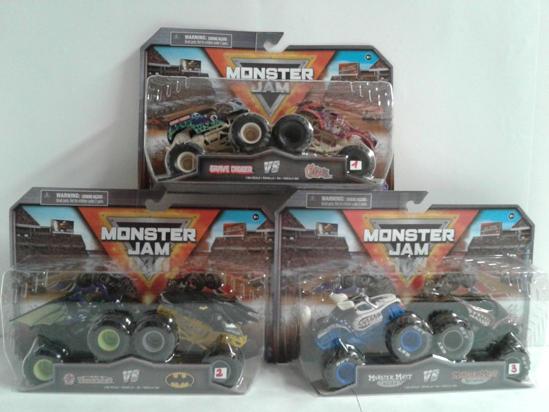 May include: Monster Jam toy trucks in their packaging. The trucks are in clear plastic packaging with cardboard backing. The trucks include Grave Digger, El Toro Loco, Batman, and Monster Mutt. The packaging features the Monster Jam logo.