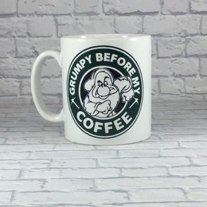Könnte beinhalten: Weiße Keramik-Kaffeetasse mit einer grünen und schwarzen Grafik eines Comic-Charakters mit dem Text "Grumpy Before My Coffee".