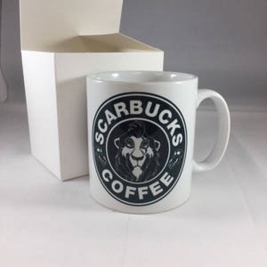 May include: A white ceramic coffee mug with a black and white logo that says "Scarbucks Coffee". The logo features a lion's head with a mane.