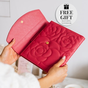 Peut inclure: Un carnet en cuir rose avec un motif de roses et des accents dorés. Le carnet est ouvert pour révéler un intérieur vierge. Le carnet est livré avec un carnet assorti gratuit.