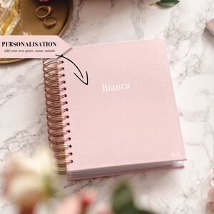 May include: A light pink spiral-bound notebook with the name "Bianca" printed in white. The notebook has a rose gold spiral binding and the initials "B.S." are printed on the bottom right corner. The text "PERSONALISATION add your own quote, name, initials" is also visible.
