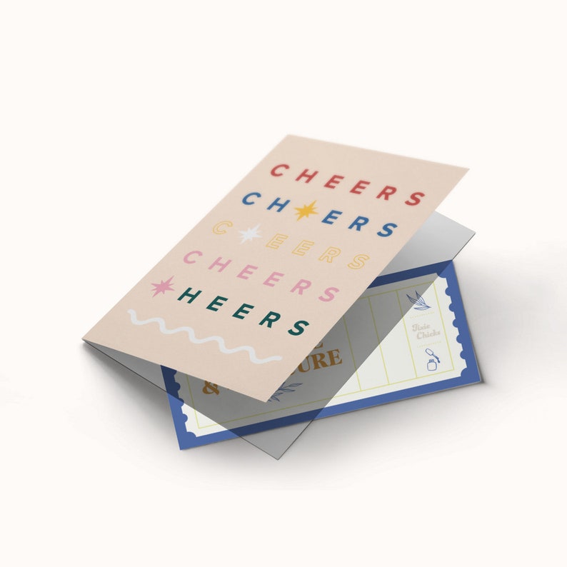May include: A folded card with a pink background and the word "CHEERS" repeated in different colours and fonts. The card is folded over a blue and white ticket with the text "Taste Chicken" and a small bird graphic.