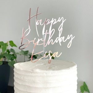 May include: A white cake with rose gold glitter cake topper that says "Happy Birthday Eisa".