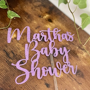 May include: Purple glitter cake topper with the text "Martha's Baby Shower" in a cursive font.