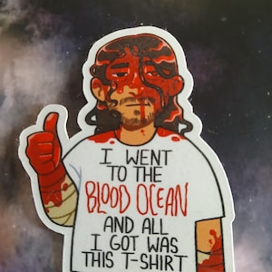 Puede incluir: Una pegatina con una ilustración de dibujos animados de una persona cubierta de sangre roja, haciendo una señal de pulgar hacia arriba. La persona lleva una camiseta blanca con el texto "I went to the Blood Ocean and all I got was this T-shirt."
