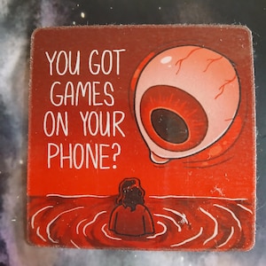 Puede incluir: Un posavasos cuadrado rojo con el texto "YOU GOT GAMES ON YOUR PHONE?" y una ilustración de un ojo gigante y una persona en el agua. El posavasos tiene un aspecto vintage y desgastado.